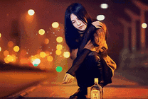 伤心的女孩蹲在马路边面前放着一瓶白酒gif图片