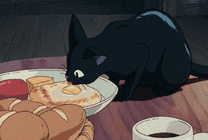 可爱的小黑猫站在桌子上舔面包吃gif图片