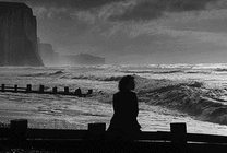 伤心的女孩坐在海边的石栏上看浪花gif图片