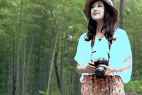漂亮的女孩拿着相机戴着帽子走在树林里gif图片